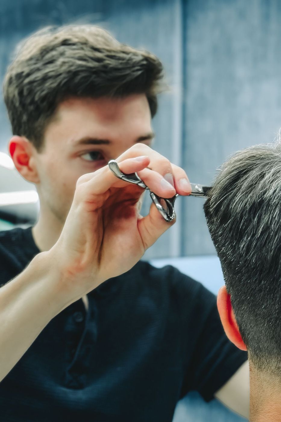 Barbeiro aparando o cabelo de um cliente com tesoura, visto por cima do ombro