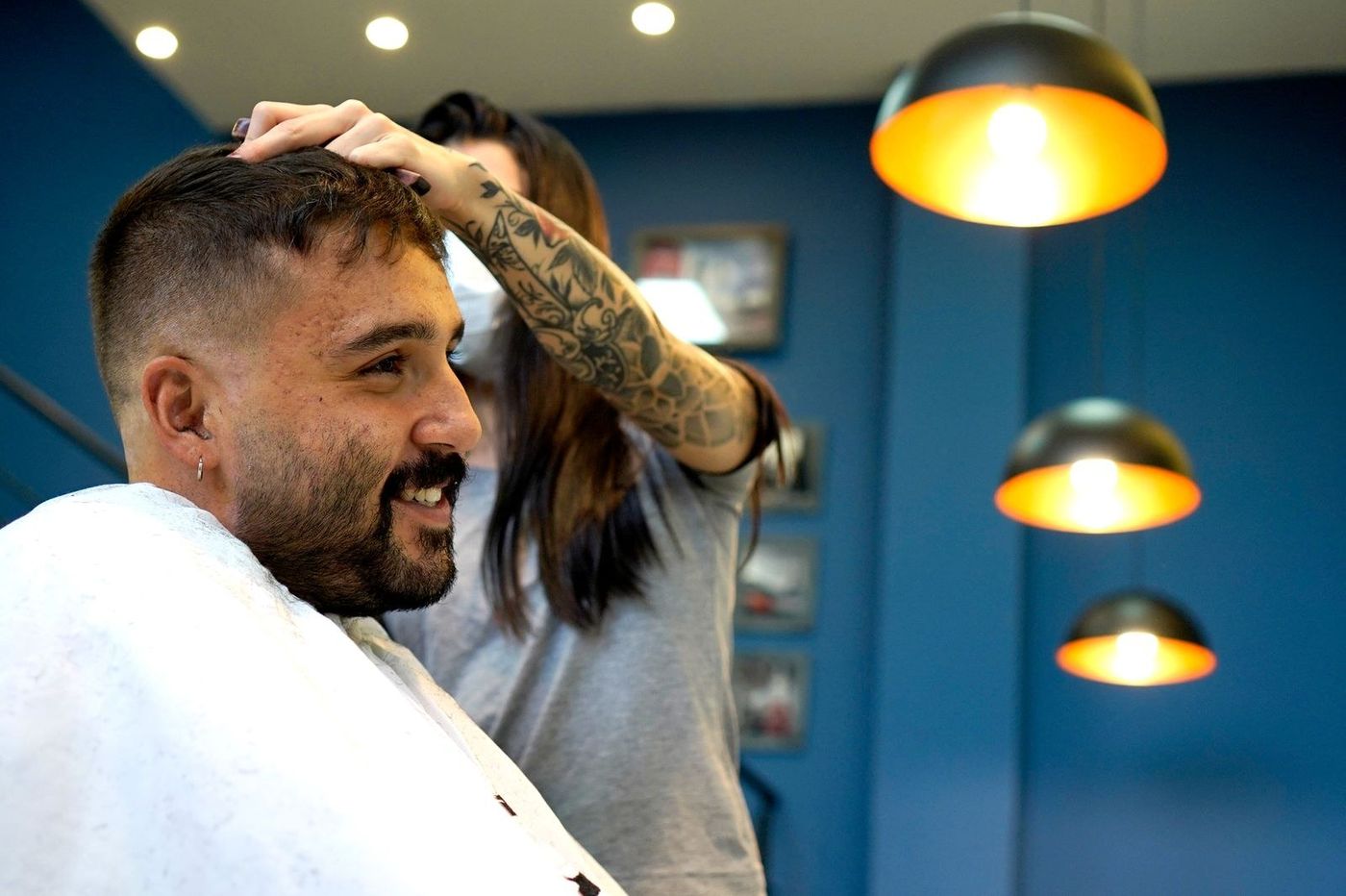 Cliente sorrindo na cadeira enquanto a barbeira ajeita o cabelo dele